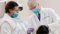 Oral surgeon treats patient while post-doctorate student watches.